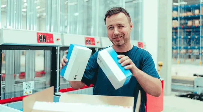 A worker adds inventory to a box for order fulfillment