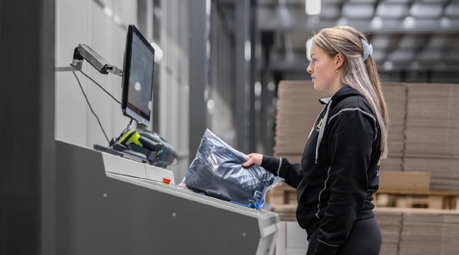 A warehouse worker at an AutoStore workstation in an automated warehouse