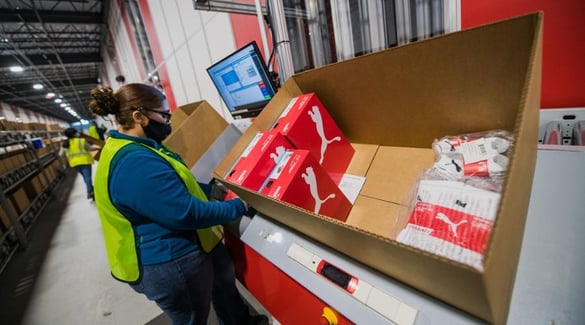 A worker adds inventory to shipping box at PUMA