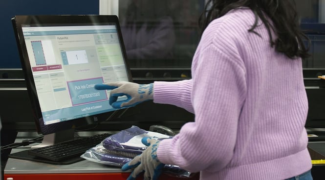 A worker taps a computer screen at an AutoStore workstation