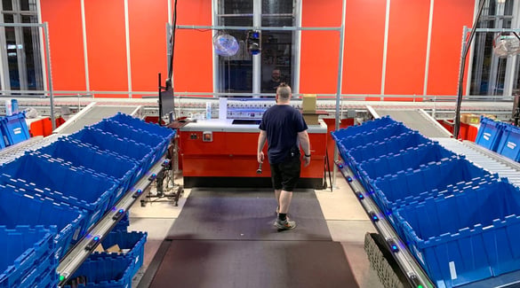 A worker walking toward workstation between order bins