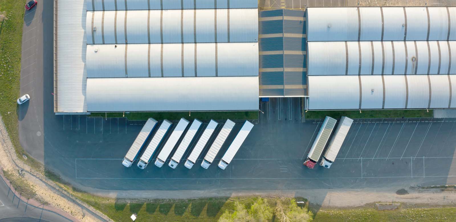 The exterior view of a warehouse seen from above with trucks and one little car parked outside 